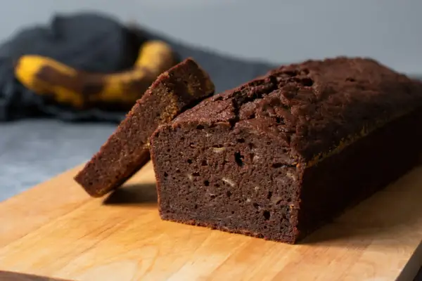 En saftig banankaka med choklad, en skiva är uppskuren. I bakgrunden syns en övermogen banan.
