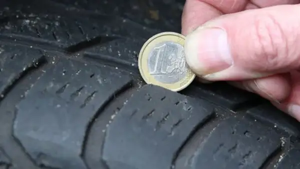 Nahaufnahme eines Reifens, auf dem eine 1-Euro-Münze zur Messung der Profiltiefe liegt.