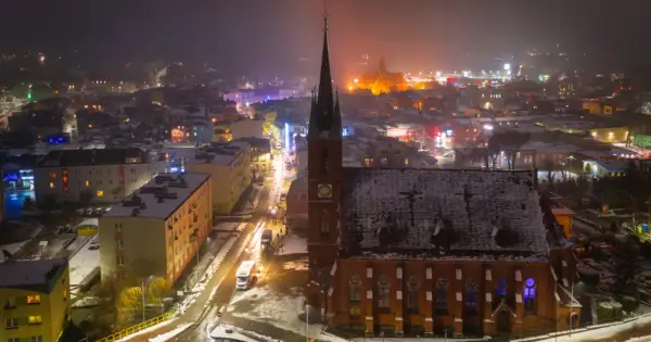 Nocna panorama Kościerzyny, ośnieżona trasa miejska z kościołem w centrum i rozświetlonymi budynkami.