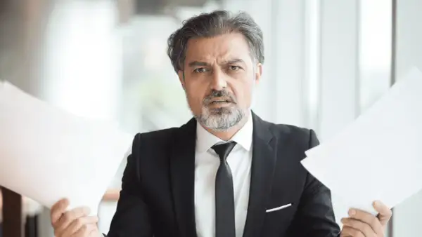 Hombre con traje y papeles, preocupado por cuanto cobra una inmobiliaria por alquilar un piso.