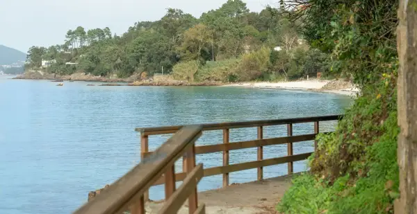 Camino de madera hacia la playa Mogor, con el mar azul y la costa verde al fondo.