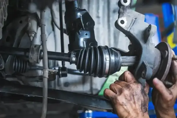 Mechanik sprawdza przegub zewnętrzny w samochodzie. Widać gumową osłonę i metalowe elementy.