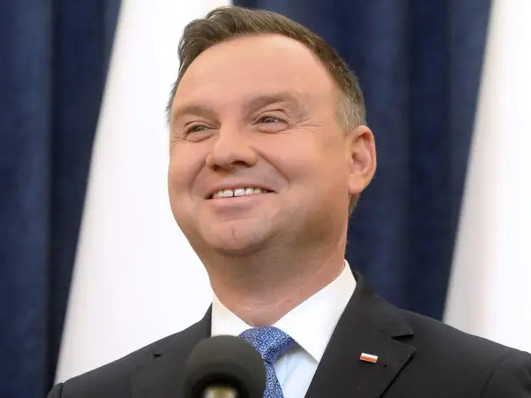 Uśmiechnięty Andrzej Duda, jego wiek nie jest widoczny na zdjęciu, ale wygląda na dojrzałego mężczyznę w garniturze.
