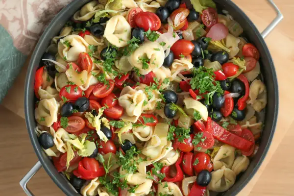 Kolorowa sałatka z tortellini, pomidorkami koktajlowymi, czarnymi oliwkami, papryką i natką pietruszki w patelni.