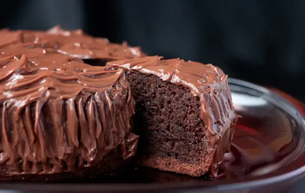 Una fetta di torta al cioccolato, soffice e umida, ricoperta da una glassa al cioccolato lucida e cremosa.