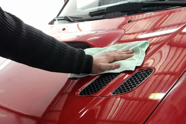 Ręka z mikrofibrą czyści czerwony lakier. Dowiedz się, czym usunąć asfalt z samochodu domowym sposobem, by przywrócić mu blask.