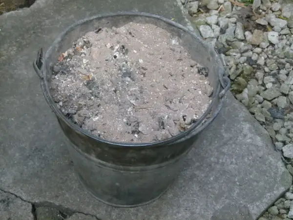 Metalowy kubeł wypełniony popiołem z węgla, który może posłużyć jako cenny nawóz do ogrodu.