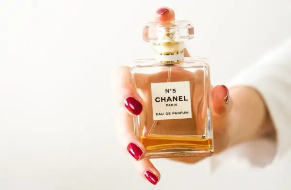 Dłoń z czerwonymi paznokciami trzyma flakon Chanel N°5. Czy perfumy mają datę ważności?