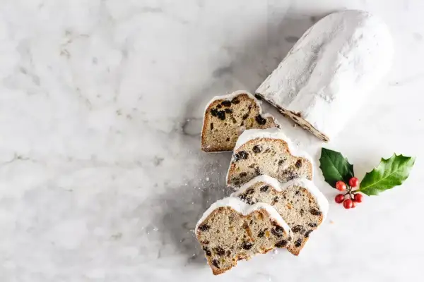Le stollen, un délice de Noël, est saupoudré de sucre glace. Des tranches révèlent des fruits secs et des baies rouges sur une branche de houx.