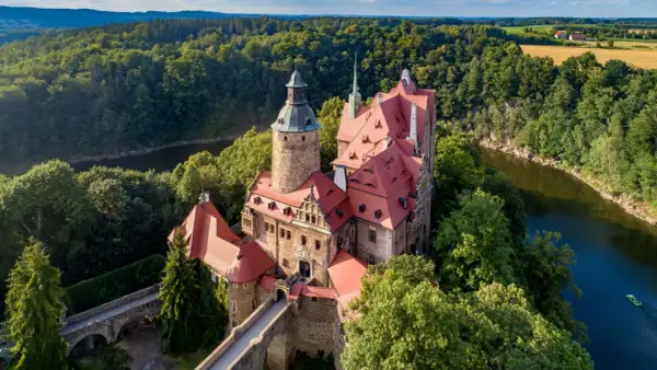 Zamek Czocha, malowniczo położony nad rzeką, otoczony bujną zielenią.