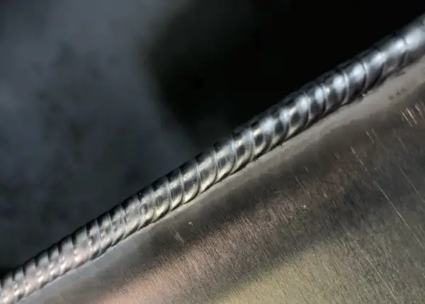 Precyzyjne spawanie aluminium migomatem. Widoczny gładki, lśniący ścieg spawalniczy na metalowej powierzchni.