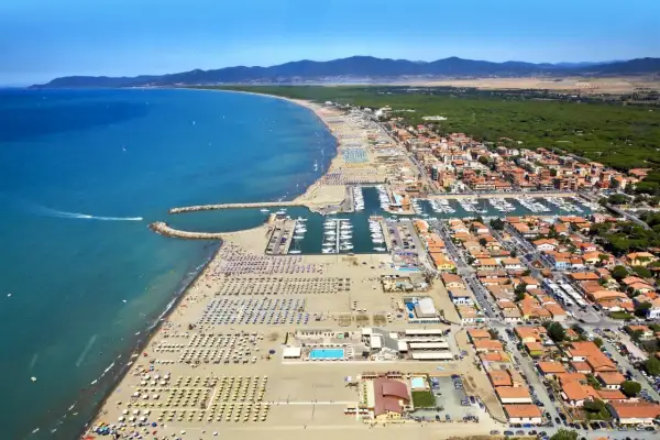 Vista aerea di una località balneare in provincia di Grosseto, con spiaggia attrezzata, porto turistico e case con tetti rossi.