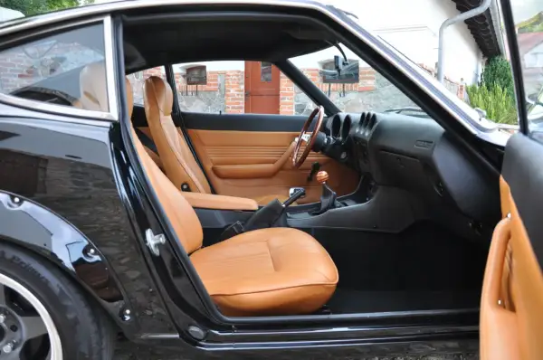 Wnętrze klasycznego Datsuna 280Z z brązową skórzaną tapicerką i drewnianą kierownicą.