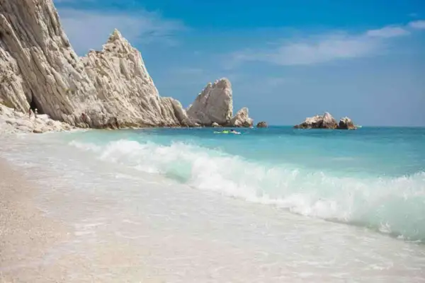 Spiaggia delle Due Sorelle: onde turchesi lambiscono la riva, rocce bianche imponenti si ergono sul mare azzurro, un paradiso incontaminato.