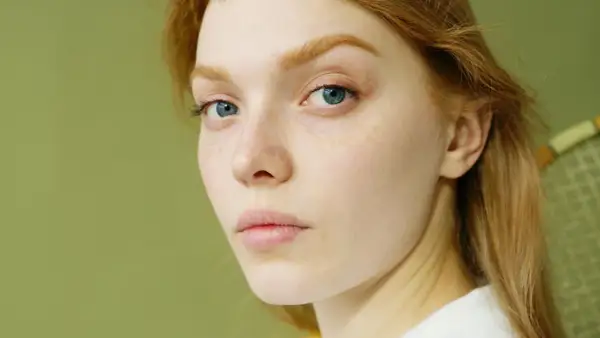 Rostro de mujer joven con pecas y ojos azules. Su cabello es pelirrojo. ¿Glicación qué es? Podría afectar la piel.