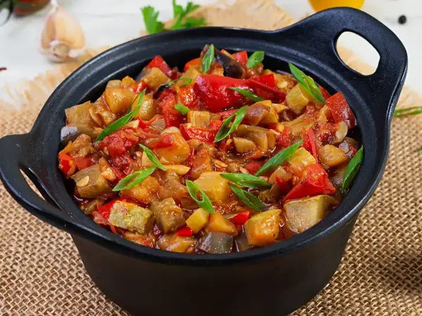 Un plat de ratatouille colorée, avec des morceaux d'aubergine, de courgette, de poivron rouge et de tomate, garni de ciboule fraîche. Une recette savoureuse.