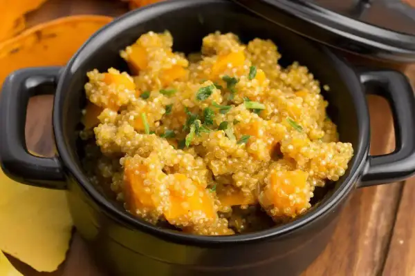 Un saporito piatto di quinoa e zucca, guarnito con erbe fresche, servito in una ciotola nera.