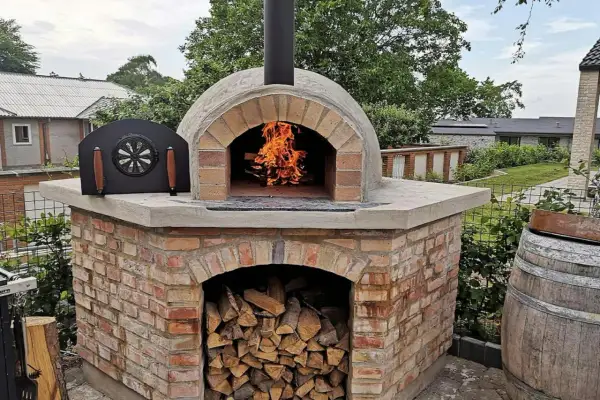 En vacker, murad pizzaugn med eld som sprakar i öppningen. Ved ligger staplad under ugnen, redo för nästa pizzakväll.