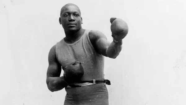 A boxer in an old boxing stance, wearing a tank top and shorts, with gloves on both hands, ready to fight.