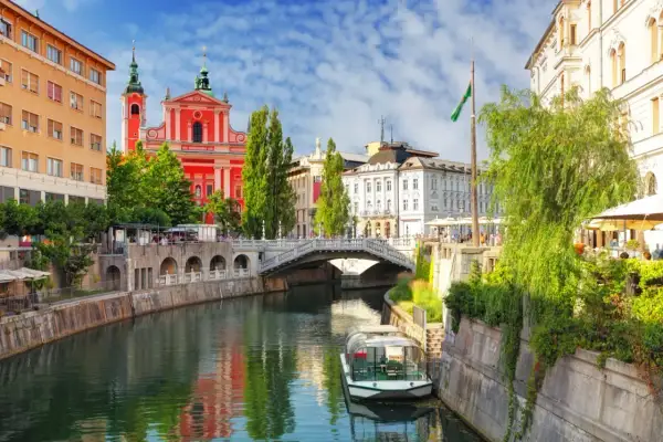 Lublana atrakcje: rzeka Ljubljanica, Most Potrójny, kościół Franciszkanów i łódź wycieczkowa.