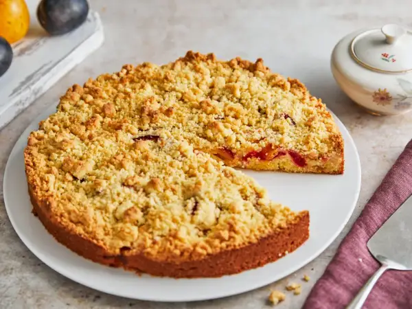 Ein saftiger Streuselkuchen mit Obst, bedeckt mit goldbraunen Streuseln, wartet darauf, angeschnitten zu werden.
