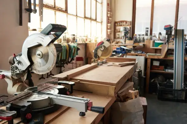 Un atelier menuiserie maison avec des scies circulaires, des établis et des outils. Des planches de bois sont prêtes pour être travaillées.