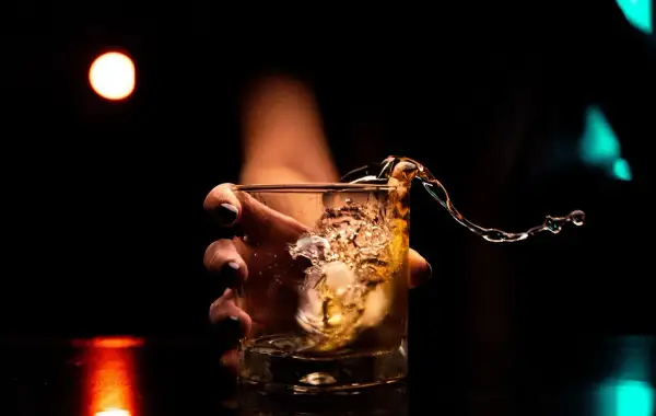 Dłoń trzyma szklankę z whisky, gdy płyn rozlewa się, tworząc falę. Kto wydaje koncesję na alkohol, by móc cieszyć się takimi chwilami?