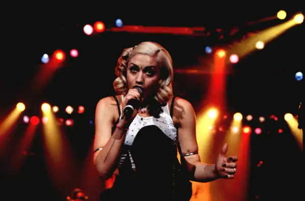 Gwen Stefani śpiewa na scenie, otoczona kolorowymi światłami.