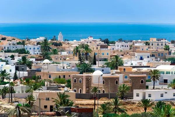 Piękne, białe domy z niebieskimi okiennicami i palmami na tle błękitnego morza. Idealna pogoda Djerba.