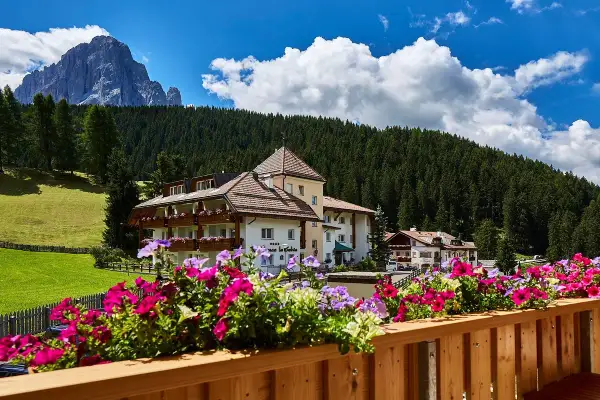 Fiori colorati su un balcone con vista su un hotel e le montagne, un'oasi di pace nei rifugi Val Gardena.