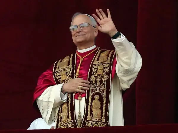 Papież w bogato zdobionej szacie pozdrawia wiernych. Jego uśmiech i gest ręki budzą nadzieję, a jego strój przypomina o tym, skąd pochodzi papież i jego dziedzictwo.