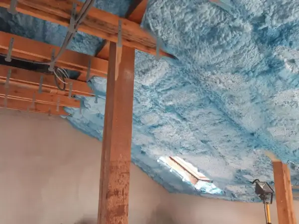 Piana na poddasze tworzy izolacyjną warstwę na drewnianej konstrukcji dachu, z widocznym oknem dachowym.