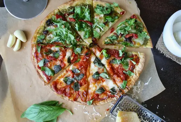 Pizza podzielona na pół: jedna połowa z pesto i rukolą, druga z sosem pomidorowym i bazylią.