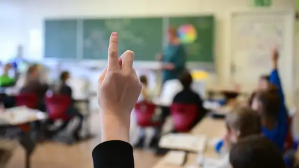 Ein Schüler hebt die Hand im Unterricht. Seit wann gibt es die Schulpflicht in Deutschland? Die Antwort liegt im Dunkel der Geschichte, aber die heutige Schulpflicht ist ein Meilenstein.