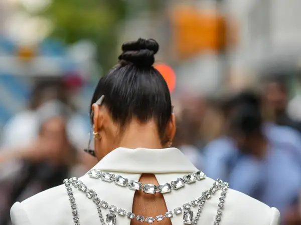 Capelli raccolti in un elegante chignon alto, impreziositi da una collana scintillante su un abito bianco.