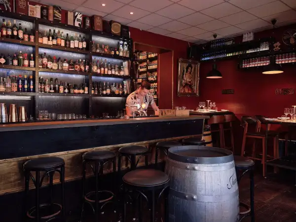 En bar med hyllor fyllda med flaskor, en bardisk med pallar och en bartender. En perfekt plats för vinbarer Stockholm.