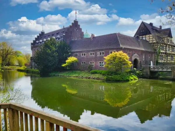 Schloss Wittringen, ein imposantes Backsteingebäude, spiegelt sich im Wasser eines umliegenden Grabens.