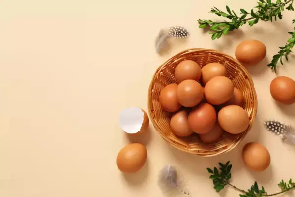 Koszyk pełen jajek, piórka i gałązki zieleni. Widać też skorupkę po jajku. Makro zbliżenie na naturalne piękno.