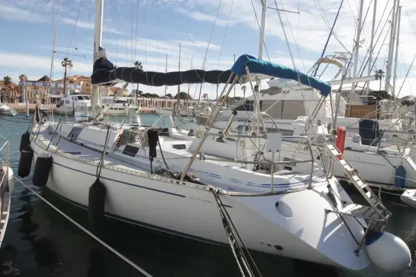 Barche a vela ormeggiate in un porto, con la scritta "Genesi Sport" su una di esse. Cielo azzurro con nuvole.
