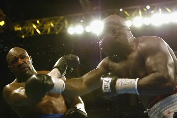 Two boxers clash under bright lights. The sound of their punches echoes, a testament to the force behind each blow.
