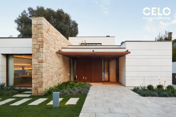 Casa moderna con acabados de fachadas de piedra y paneles blancos. Un camino de baldosas conduce a la entrada principal de madera.