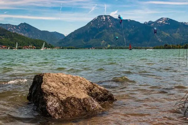 Kitesurfer tanzen über das Wasser am Bad Wiessee, während Segelboote und Berge im Hintergrund ruhen.