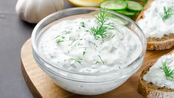 Un bol de salsa de yogur con eneldo y pepino, listo para untar en pan tostado.