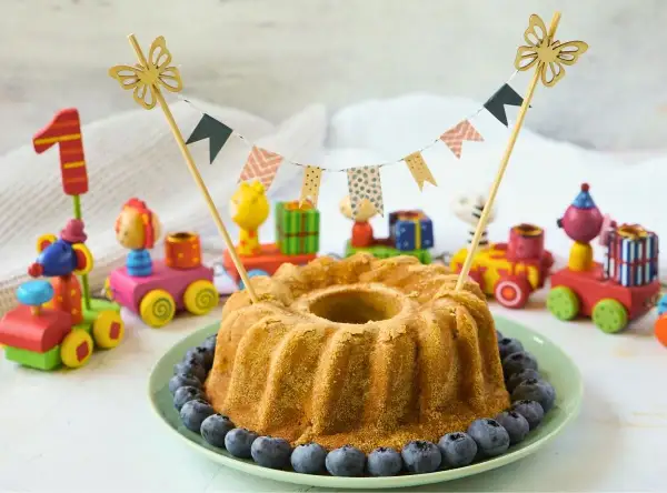 Saftiger Kuchen ohne Zucker für Kinder, dekoriert mit Blaubeeren und bunten Holzspielzeugen. Perfekt für den ersten Geburtstag!
