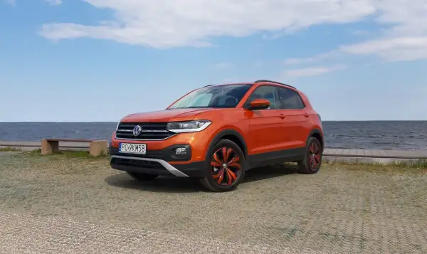 Pomarańczowy Volkswagen T-Cross stoi nad jeziorem, gotowy na letnią przygodę.