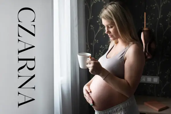 Ciężarna kobieta z kubkiem czarnej herbaty w dłoni, spogląda przez okno. Delikatne światło podkreśla jej brzuszek.
