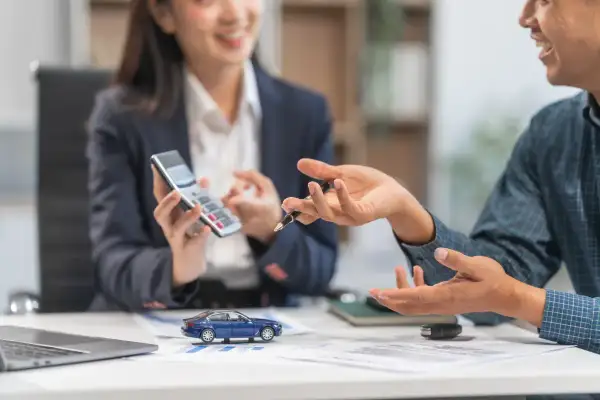 Rozmowa o tym, leasing co to. Kobieta z kalkulatorem i mężczyzna gestykulujący przy biurku z modelem samochodu.