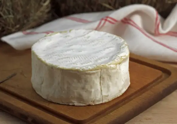Un delicioso queso francés, con su corteza blanca y cremosa, descansa sobre una tabla de madera.
