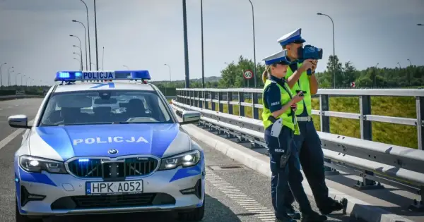 Policjanci kontrolują prędkość na drodze. Obok radiowóz z włączonymi sygnałami. Bezpieczne prowadzenie pojazdu to priorytet.