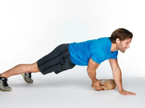 Man performing an around the world plank exercise, balancing on one hand and a paper bag.